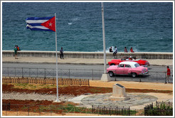 Cuban flag and pink and red cars on the Malec&oacute;n.