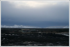 Volcanic terrain with metal hut and and snow-covered mountains.
