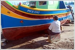 Man varnishing his boat next to Marsaxlokk Bay.