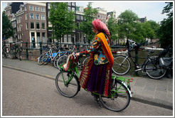 Colorfully dressed woman riding bicycle.  Bridge over Singel canal, Centrum district.